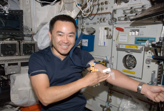 Astronaut aboard space shuttle with arm extended demonstrating where IV goes in inside elbow