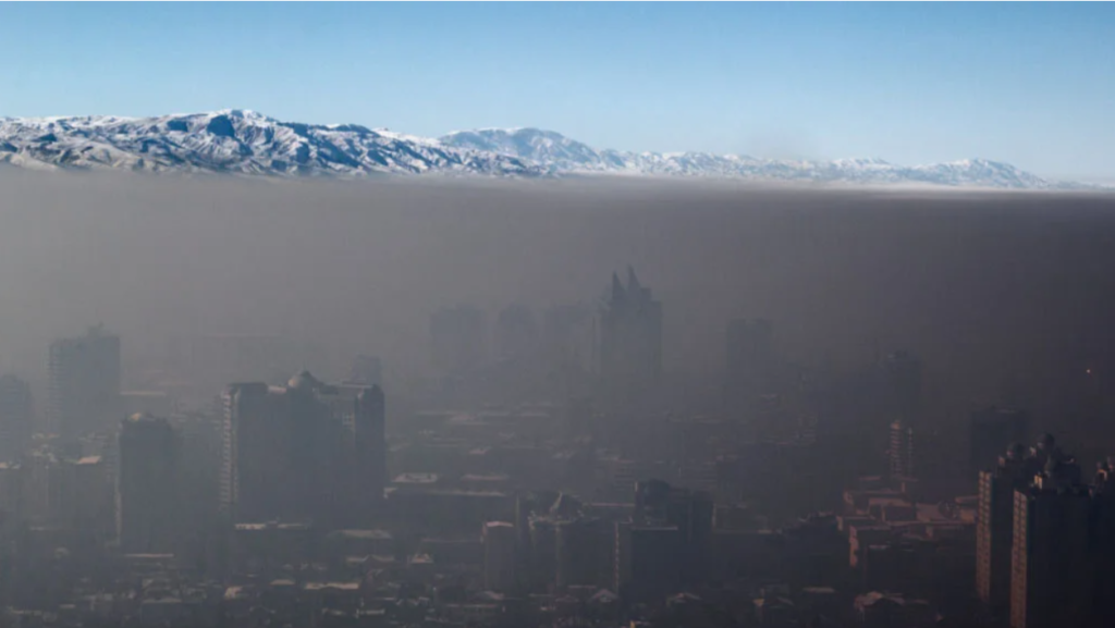 smog over Almaty, Kazakhstan showing deep brown haze over city with snow-capped mountains and blue sky in distance